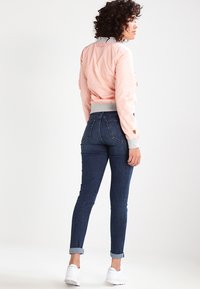 Giacca bomber rosa con polsini e colletto a coste, abbinata a jeans blu scuro. Sneakers bianche completano il look.