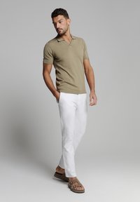 Korte mouwen olijfgroene polo, slim-fit witte broek en bruine instapschoenen. D magasine textuur met een kraag en minimale ontwerpelementen.