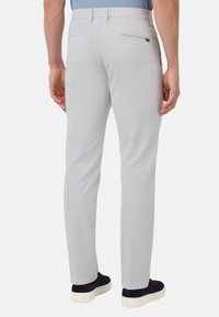 Svetlo sivi hlače s slim fit krojem, z ravnim sprednjim delom, zadnjimi žepih z zadrgo in gladko teksturo. Obute z temnimi čevlji.