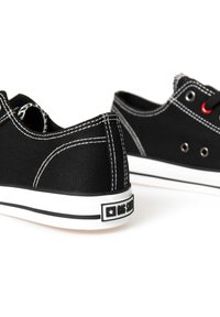 Zapatillas de lona negras con costuras blancas en contraste, puntera redonda, suela de goma blanca y ojales rojos; logotipo en la lengüeta del talón.