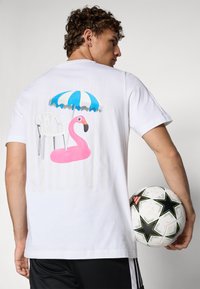 Hvid bomulds t-shirt med et grafisk motiv af en pink flamingo og en strandparasol på ryggen. Designet er livligt med legende sommerelementer.