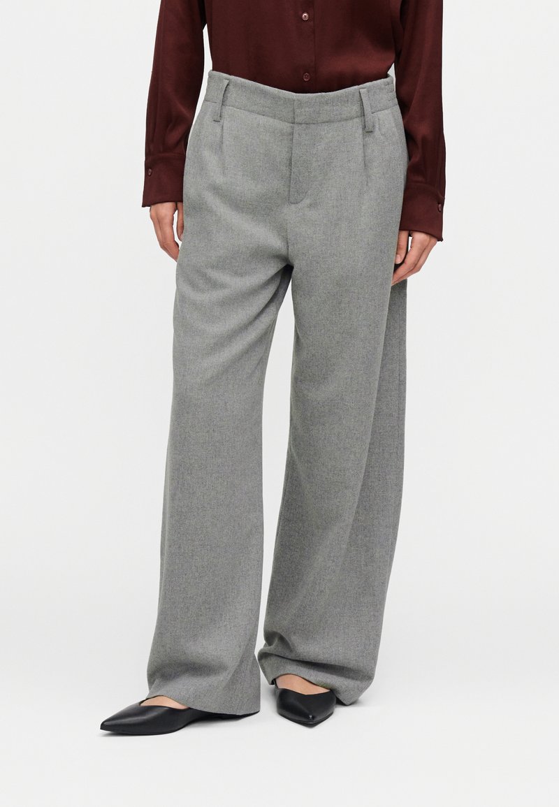 Pantalon gris à jambes larges avec une finition texturée, doté d'une taille haute et de poches latérales. Associé à une chemise bordeaux à manches longues et des chaussures noires sans lacets.