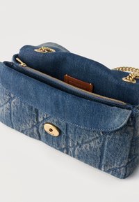 Μικρό μπλε τζιν καπιτονέ πορτοφόλι με χρυσή αλυσίδα λουρί και τσέπη με φερμουάρ, μερικώς ανοιχτό που δείχνει καφέ δερμάτινη ετικέτα Coach στο εσωτερικό.