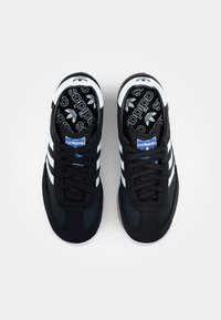 Zwarte sportieve schoenen met witte strepen, met een gestructureerde bovenkant, vetersluiting en een patroon in de binnenzool. Rubberen zool met een ronde neus.