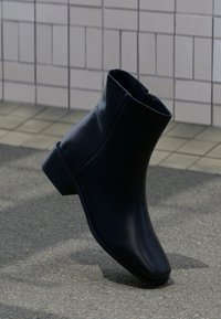 Bottine noire en cuir lisse, avec un bout carré et un petit talon empilé. Fermeture zippée sur le côté intérieur.