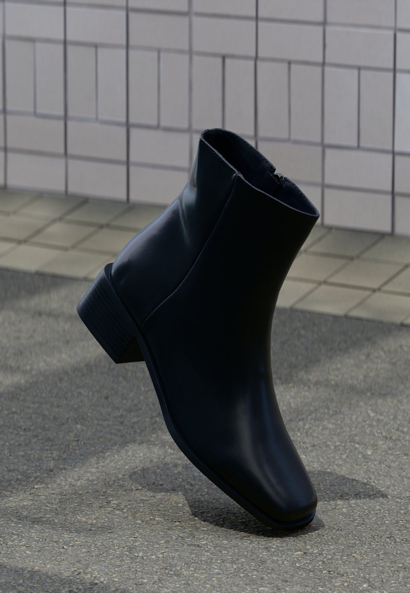 Bottine noire en cuir lisse, avec un bout carré et un petit talon empilé. Fermeture zippée sur le côté intérieur.