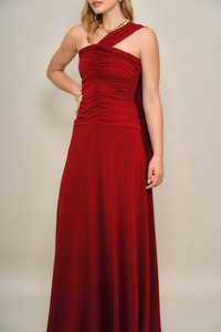 Κόκκινο βραδινό φόρεμα με σχεδιασμό ενός ώμου, κορσάζ με ρυτίδες, μακριά ρέουσα φούστα και απαλή υφή υφάσματος. Διακοσμημένο με ελάχιστα κοσμήματα.
