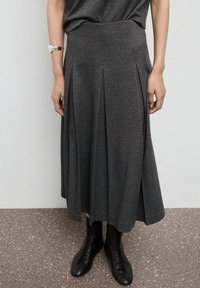 Jupe plissée grise avec une taille ajustée et un tissu fluide qui tombe mi-mollet, associée à des bottines noires à lacets.