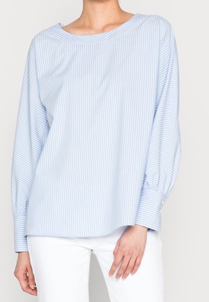 Light blue and white vertically striped long-sleeve blouse with wide cuffs, worn with white pants on a standing person.