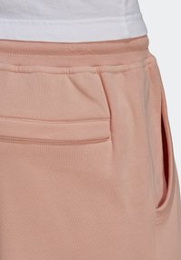 Close-up of light pink sweatpants waistband and pocket stitching beneath a white shirt hem.