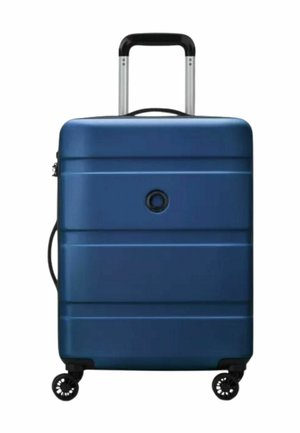 Valigia rigida blu con manico telescopico, quattro ruote girevoli e un logo circolare posizionato al centro sulla parte anteriore.