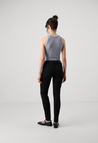 Grå ärmlös topp kombinerad med svarta skinny jeans. Toppen har en slät textur, medan jeansen har en klassisk femficksdesign.