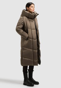 Pikk oliivroheline tikitud sulejope kõrge kraega, küljetaskute ja tõmblukudetailidega. Kandmisega mustad põlvikud.