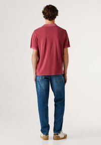 Camiseta de manga corta color granate con cuello redondo, combinada con jeans de mezclilla azul. La tela parece suave, con un ajuste relajado y un diseño minimalista.