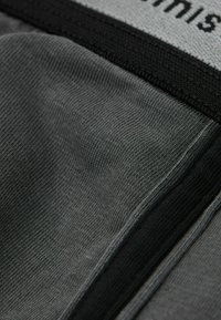 Szary materiał tekstylny z teksturowaną powierzchnią, z czarną elastyczną taśmą u góry, na której widnieje białe liternictwo.