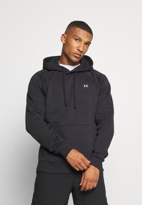 Sudadera negra con bolsillo canguro, capucha ajustable con cordón y un pequeño logo en el pecho. Fabricada con una tela suave y texturizada.