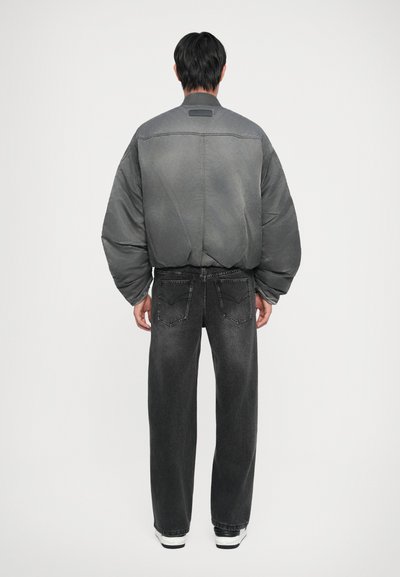 Grey bomber jacket with oversized silhouette, elastic waistband, and grey-black jeans with a faded finish and back pockets. White sneakers.