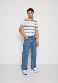 Camiseta de manga corta a rayas en azul claro y blanco, con un bolsillo; combinada con unos vaqueros de denim azul holgados y zapatillas blancas.