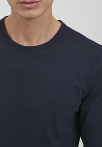 Tamno plava majica dugih rukava od mekog pamuka, s okruglim izrezom i glatkom teksturom uz jasno vidljive šavove.