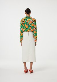 Bloemenprint blouse met lange mouwen in groen, oranje en roze; witte midi rok; rode pumps met strikdetail.