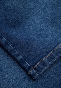Tummansininen farkkukangas, jossa on sileä pinta ja näkyvät ompeleet. Mukana taitettu helma, jossa on vaaleanruskea lanka-akkentti.