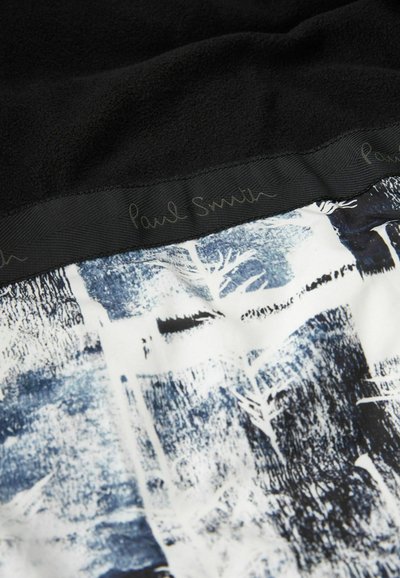 Melnas vilnas audums ar baltiem un zilajiem abstraktajiem rakstiem, kas attēlo kokus. Malu rotā melns zīds ar uzrakstu "Paul Smith".