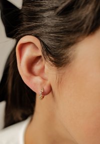 Pendientes de oro con pequeñas gemas brillantes dispuestas en un diseño curvado, descansando sobre un tono de piel claro cerca de la oreja. Textura suave.