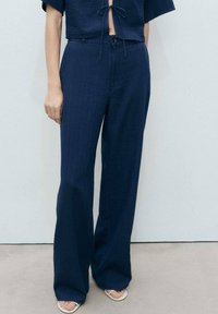 Mornarske široke hlače iz teksturirane tkanine, s sprednjim gumbom in stranskimi žepi. V kombinaciji s svetlimi natikači brez prstov.