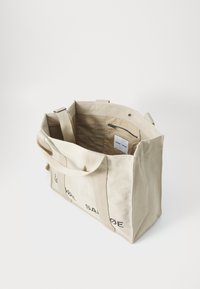 Borsa a spalla in tela beige con manici resistenti, tasca interna con zip e logo stampato. Design spazioso con una forma strutturata.