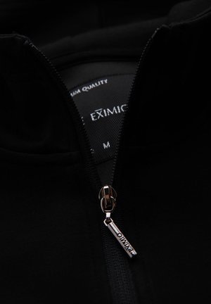 Zwarte zip-up jack van gladde stof, uitgerust met een metalen rits met een merkembleem en een binnenlabel met maat M.