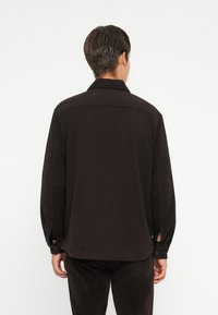 Black button-up shirt with long sleeves, a collar, and a relaxed fit. Features a smooth texture and stitching details.