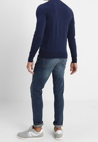 Marinblå stickad tröja, slim fit jeans och grå sneakers. Tröjan har ribbade ärmslut; jeansen har en avslappnad look med lätt slitage.