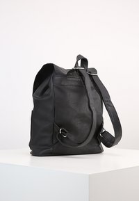 Sac à dos en cuir noir avec une forme structurée, des bretelles réglables et une poche latérale, présentant une texture lisse et un design minimaliste.