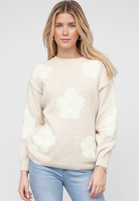 Beige gestrickter Pullover mit großen weißen Blumenmustern, Rundhalsausschnitt und gerippten Bündchen. Glatte Textur und lockere Passform.