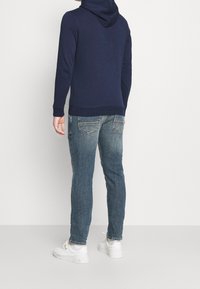 Felpa con cappuccio blu navy con polsini a costine, abbinata a jeans azzurri, vista da dietro, con dettagli di cucitura sottili e sneakers bianche.