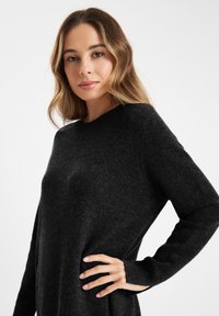 Zwarte, textuur gevende pullover trui met een ronde halslijn en lange mouwen. Het materiaal lijkt zacht en licht pluizig te zijn.