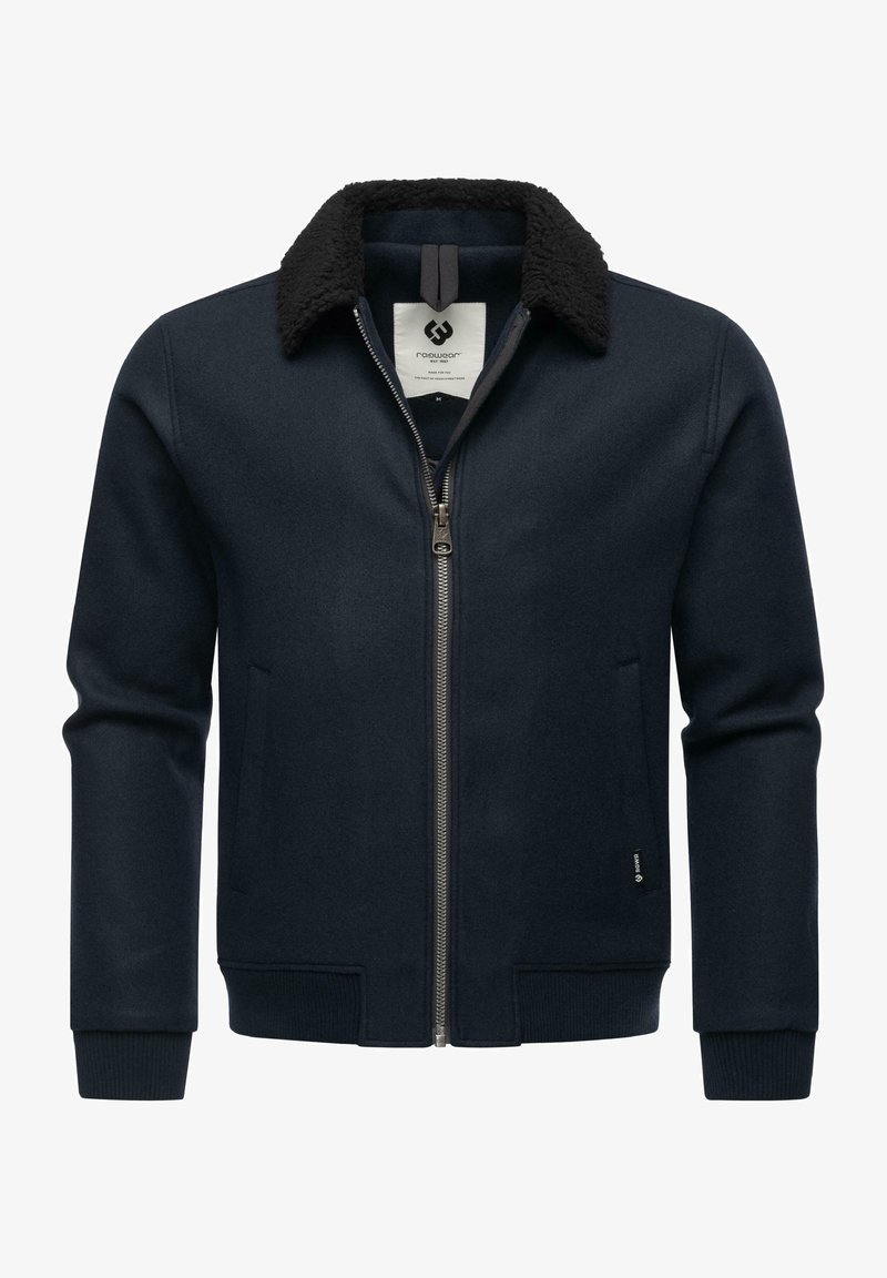 Tamsiai mėlyna striukė su užtrauktuku priekyje, su juodu dirbtiniu kailiu ant apykaklės, raukšlėtomis rankovėmis ir šoninėmis kišenėmis, pagaminta iš vilnai panašios medžiagos.