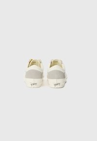 White sneakers with grey suede accents, textured canvas upper, and white rubber sole. Features a simple design with minimal branding.