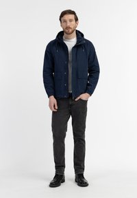 Navy blue jacket with a hood, front zipper, and two large pockets, paired with gray denim jeans and black boots. Solid textures throughout.