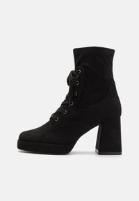 Bottes chevilles en suède noir avec un talon épais haut, fermeture à lacets à l'avant et œillets dorés. Dotées d'une texture douce et d'un col ajusté à la cheville.