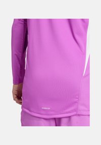 Paarse sporttop met lange mouwen gemaakt van een soepele, flexibele stof met witte accenten aan de zijkanten. Heeft een "AEROREADY" logo aan de onderzoom.