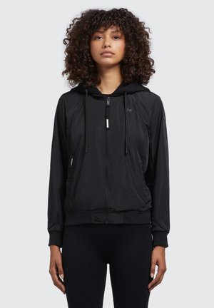 Veste zipée noire avec capuche, fabriquée en matériau léger. Elle est dotée de poches latérales, de poignets élastiques et d'une taille ajustée.