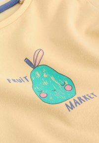 Pera verde de dibujos animados con mejillas rosas y ojos cerrados, etiquetada "Mercado de Frutas" sobre tela amarilla clara.