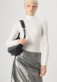 Balts ribots turtlenecks krekls un sudraba metāliska zīmuļa svārki. Melna soma ar regulējamu siksniņu turēta vienā rokā. Gludas, spīdīgas tekstūras.