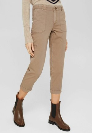 Beige cropped broek met een rechte snit, voorzien van voorzakken en gestikte accenten. Gecombineerd met bruine enkellaarsjes met elastische zijkanten.