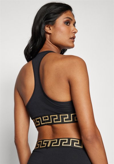 Schwarzer Sport-BH mit Racerback-Design und einem gemusterten goldenen Band am unteren Rand. Der Stoff wirkt weich und dehnbar.