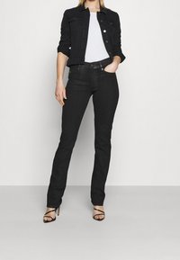 Jeans de mezclilla negros con un ajuste estrecho, que cuentan con un diseño clásico de cinco bolsillos y una cintura de altura media. Combinados con una chaqueta de mezclilla negra y una camiseta blanca.