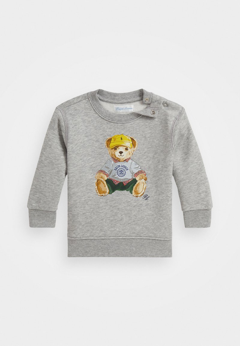 Siv sweatshirt z ilustracijo medveda v majici in kapa, z zelenimi kratkimi hlačami. Vključuje gumbe na rami.