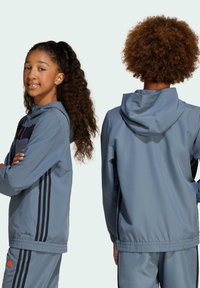 Veste de sport bleue avec zip à l'avant, capuche ajustable, accents de rayures noires et poignets élastiques aux manches et à l'ourlet. Présente le logo "AEROREADY".