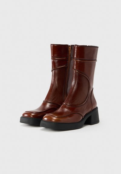 Καφέ δερμάτινες μποτάκια αστραγάλου με γυαλιστερό φινίρισμα, που διαθέτουν πλαϊνό φερμουάρ, τακούνι typu block και διακοσμητικό ραφές κατά μήκος των άκρων.